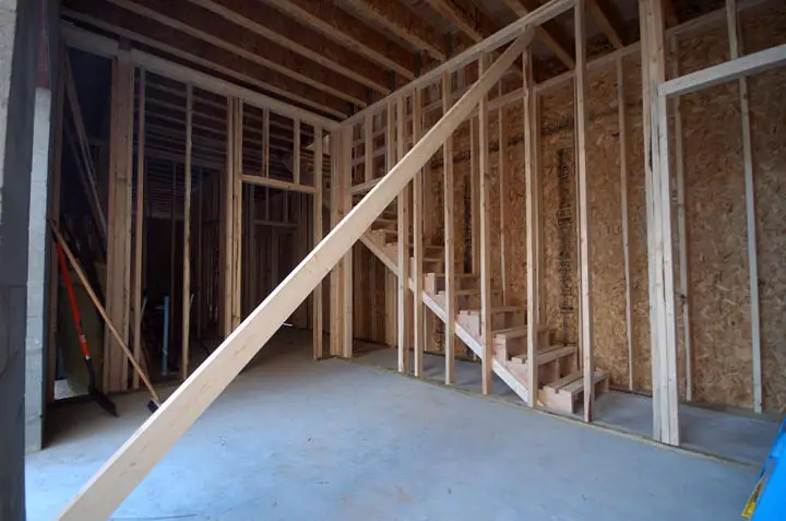 Unfinished building interior with exposed wood framing, a staircase, tools, and a large diagonal brace.