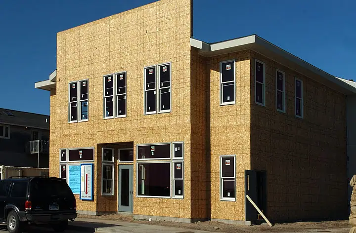 Two-story building sheathed in OSB with newly installed windows and a ground-floor entrance.