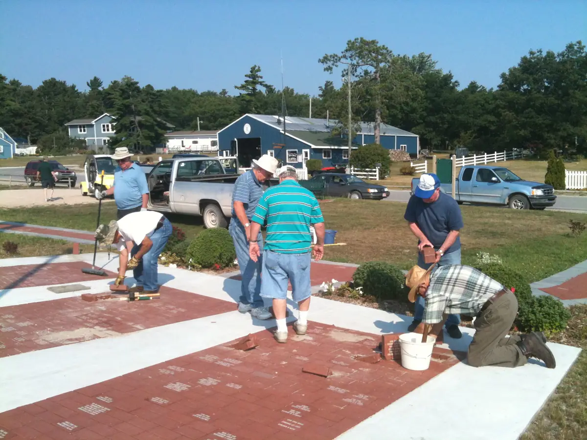 A group of people lays red paving bricks in a landscaped walkway beside a road.
