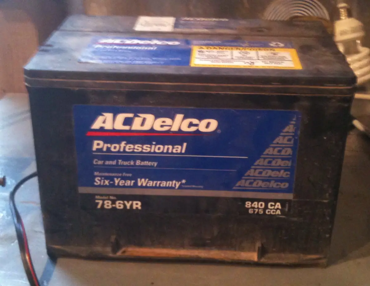 A black ACDelco automotive battery with blue branding and a yellow warning label.