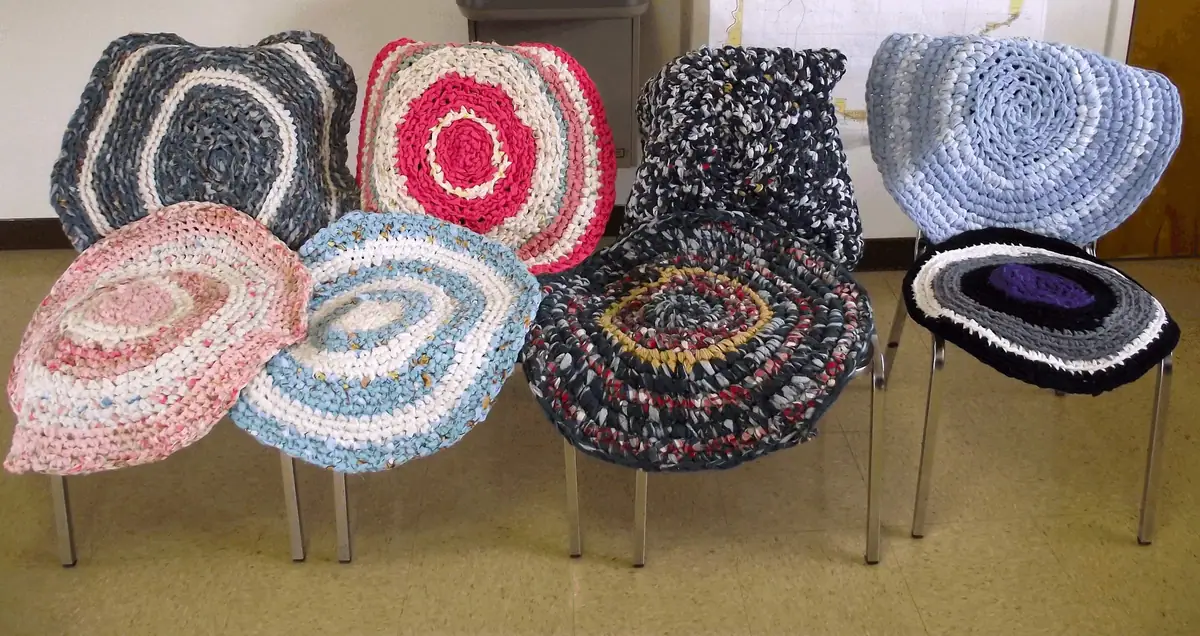 Colorful braided rag rugs are draped over chairs and displayed on a tiled indoor floor.