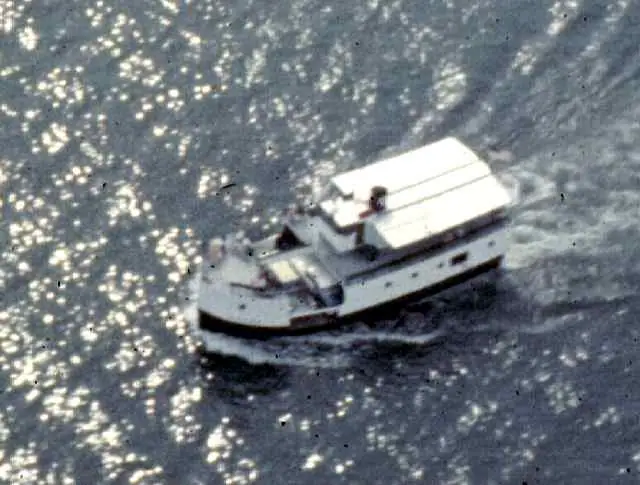 A white cabin motorboat travels across sunlit, rippling water, leaving a wake.