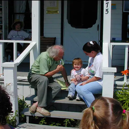 Three people sit with a small child on the steps of a white-painted porch.