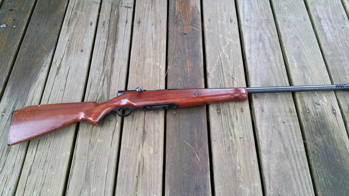 A long gun with a polished wooden stock and dark barrel rests on a weathered wooden deck.