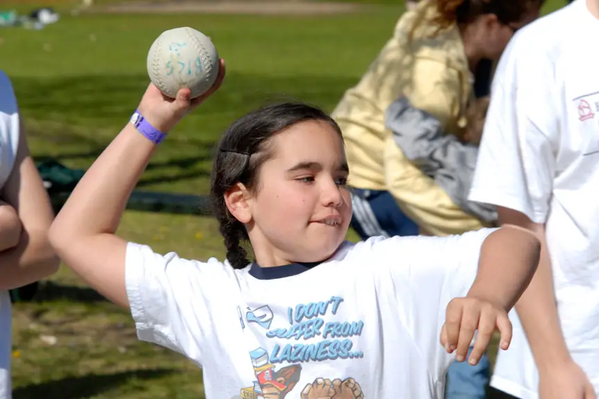 Child holding a softball in a throwing pose during an outdoor game.