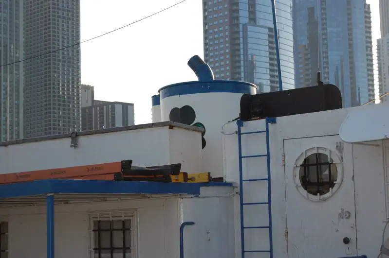 White vessel superstructure with blue trim and ladder, framed by tall glass-and-concrete towers.