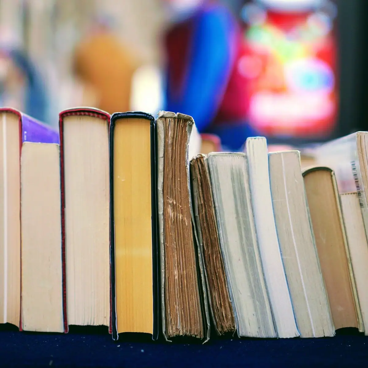 A row of worn books stands upright against a softly blurred, colorful background.