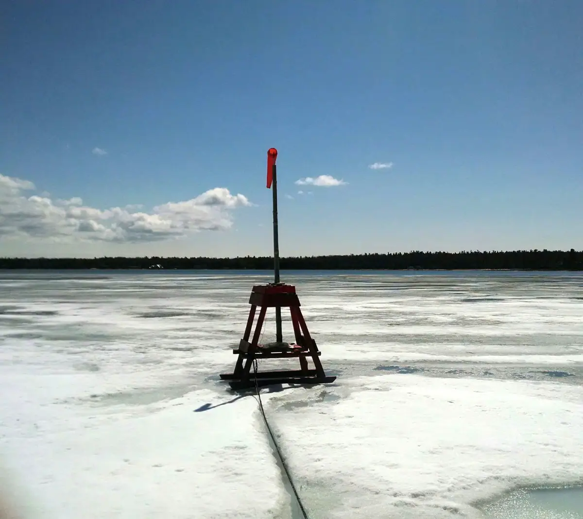 A red-topped wooden marker stands on a frozen expanse, with a rope trailing toward the camera.